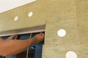 Worker installing external wall insulation around a window using mineral wool boards and fixing discs.