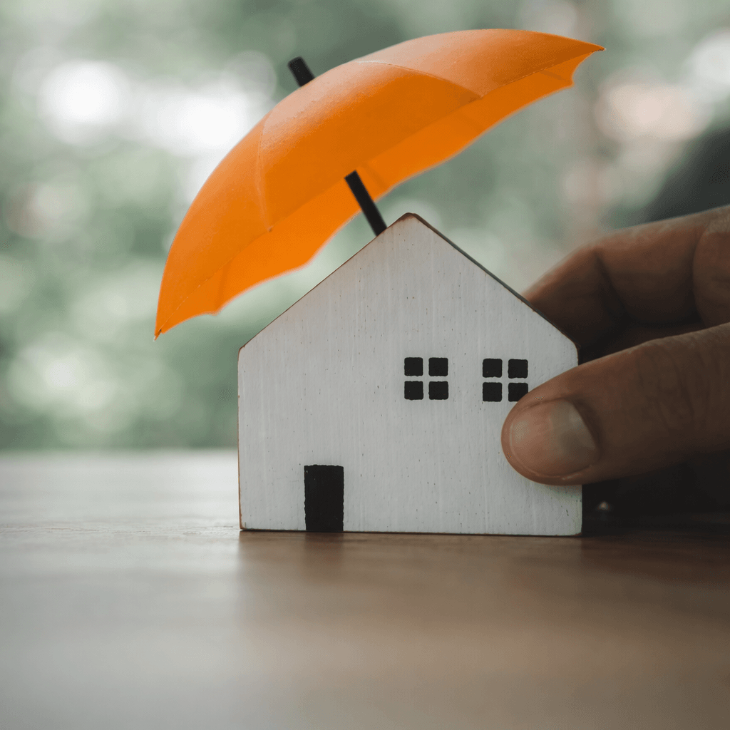 Small house model under an orange umbrella symbolising weather protection with spray cork